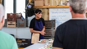 Une traiteur présente ses plats. Elle se trouve derrière une table où sont posées les assiettes.