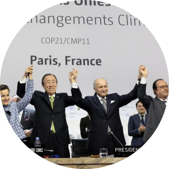 Quatre personnes sont debout et lèvent les bras en se tenant les mains. Cela se passe à la COP21 à Paris.