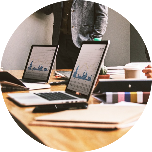 Deux ordinateurs portables sont sont posés et ouverts sur une table. Ils affichent des graphiques. Une personne est debout , derrière la table.