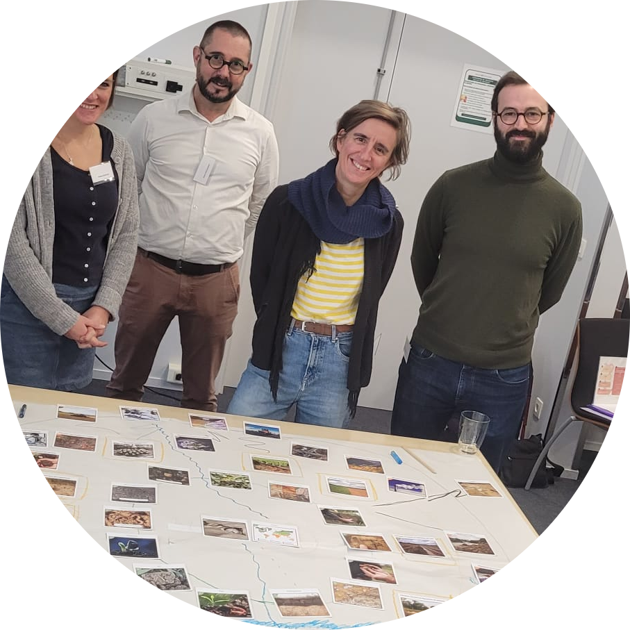 5 personnes sont debout derrière une table. Sur cette table, des cartes sont posées sur une feuille blanche.